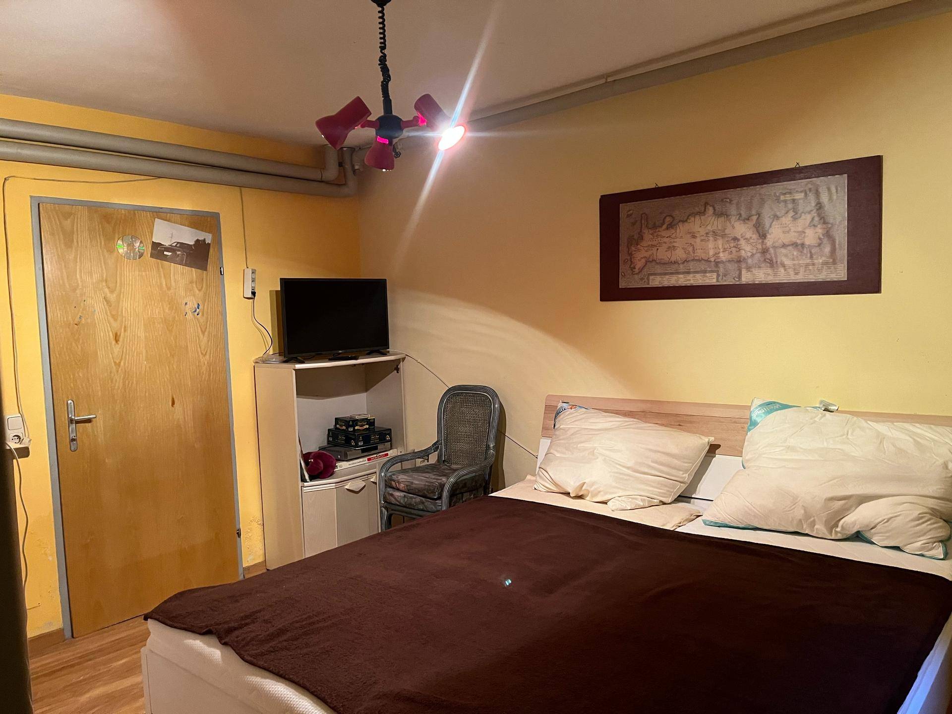 Schlafzimmer mit gelben Wänden, Doppelbett und einfacher, funktionaler Einrichtung.
