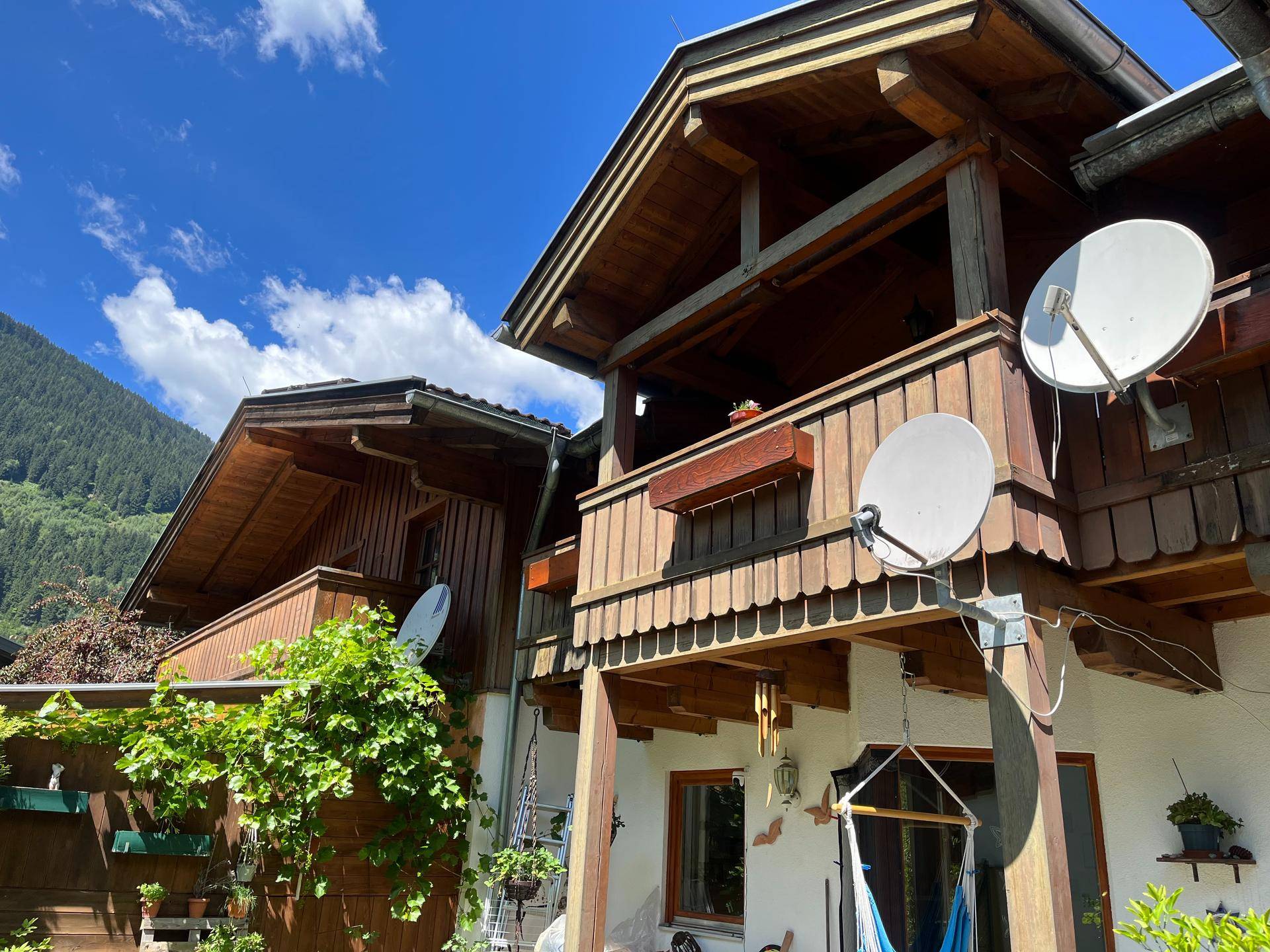 Detailansicht eines traditionellen Chalets mit Holzbalkonen und Satellitenschüsseln vor Bergkulisse.