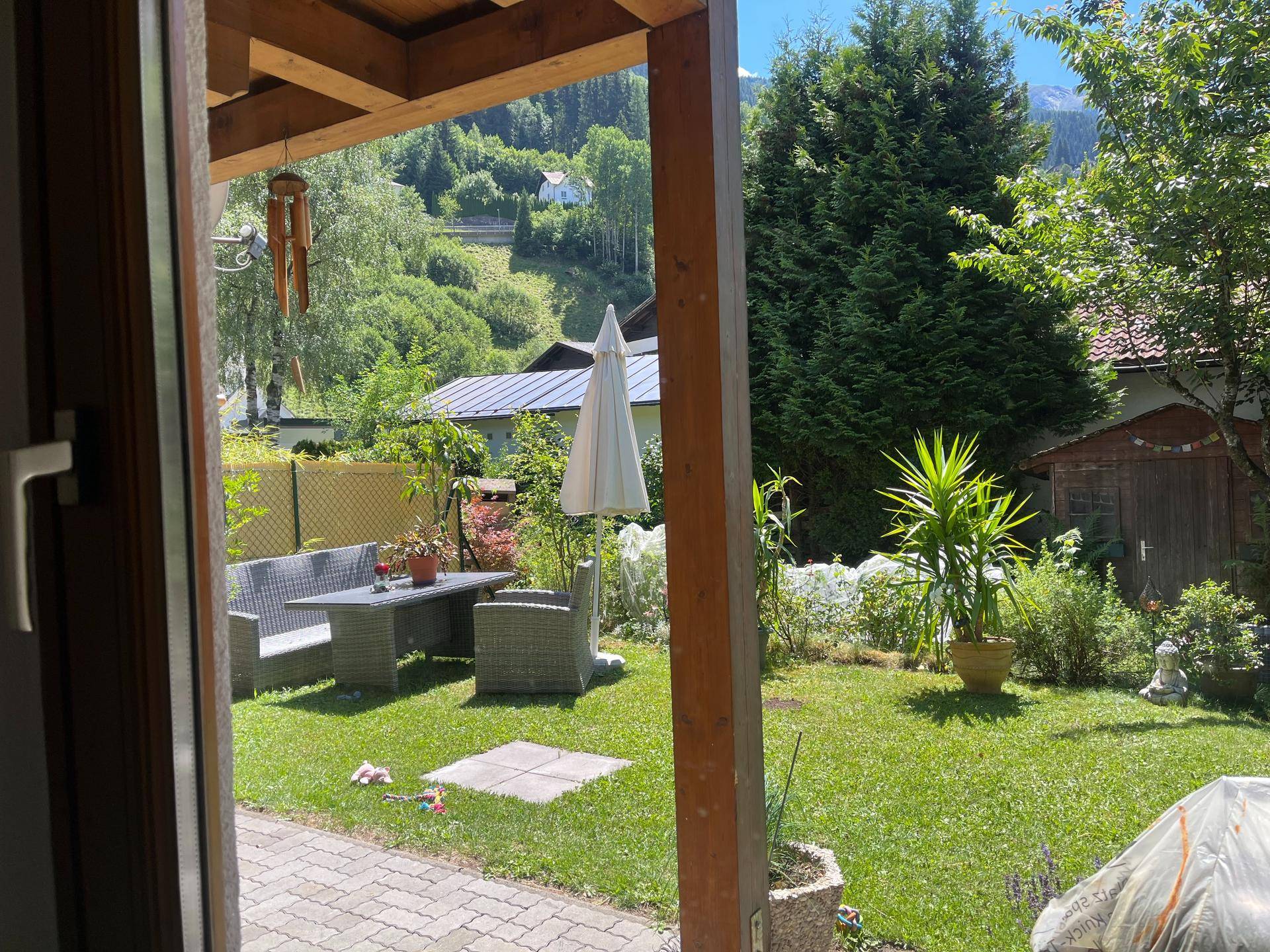 Sonniger Garten mit Terrasse, Gartenmöbeln und weitem Blick auf die grüne Berglandschaft.