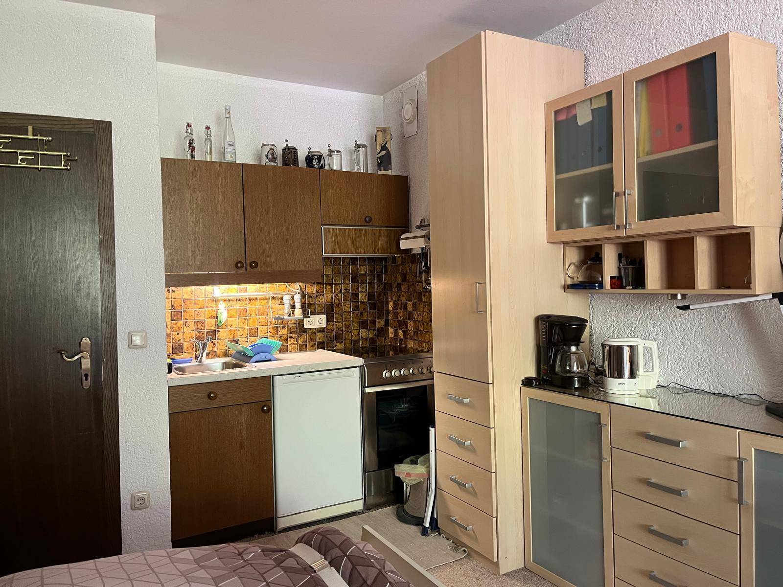 Kleine, funktionale Küche mit Holzschränken, Fliesenrückwand und grundlegenden Geräten.