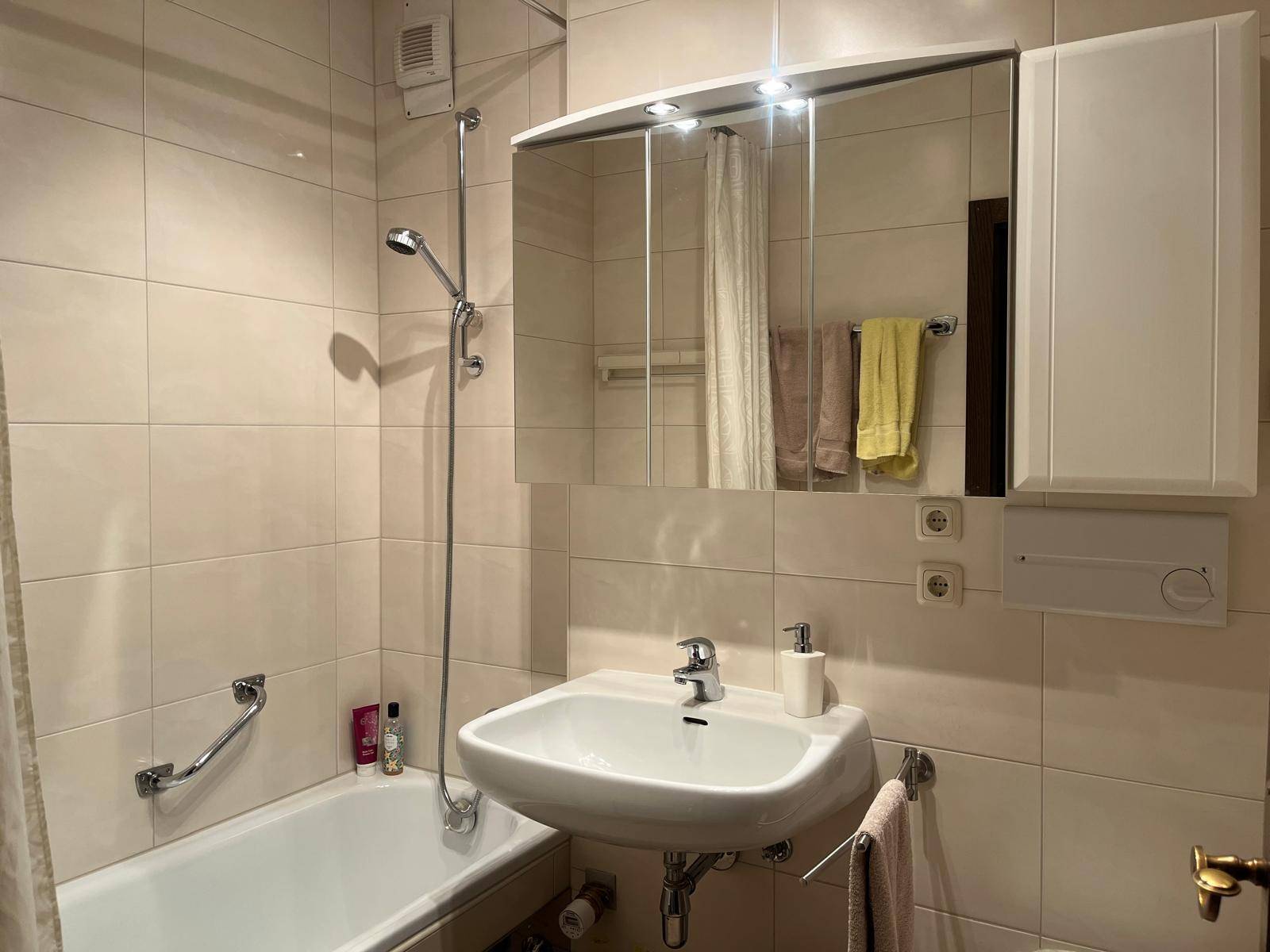 Helles Badezimmer mit Badewanne, Duschfunktion und Spiegelschrank über dem Waschbecken.