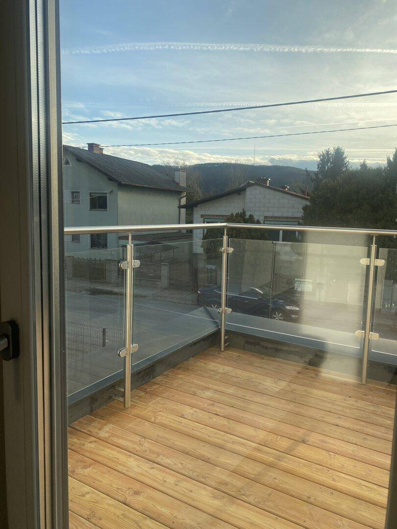 Moderner Balkon mit Holzboden und Glasgeländer, bietet einen weiten Blick auf die Umgebung.