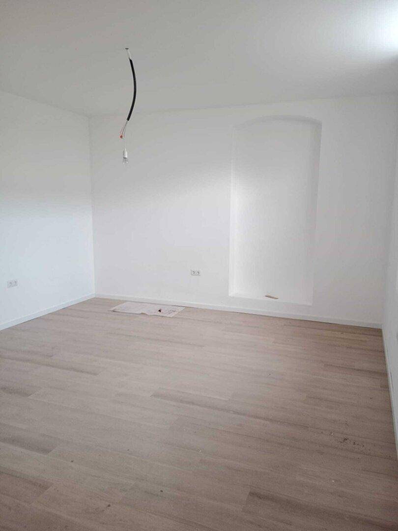 Geräumiger, heller Raum mit hellem Holzboden, weißen Wänden und einer markanten Wandnische.