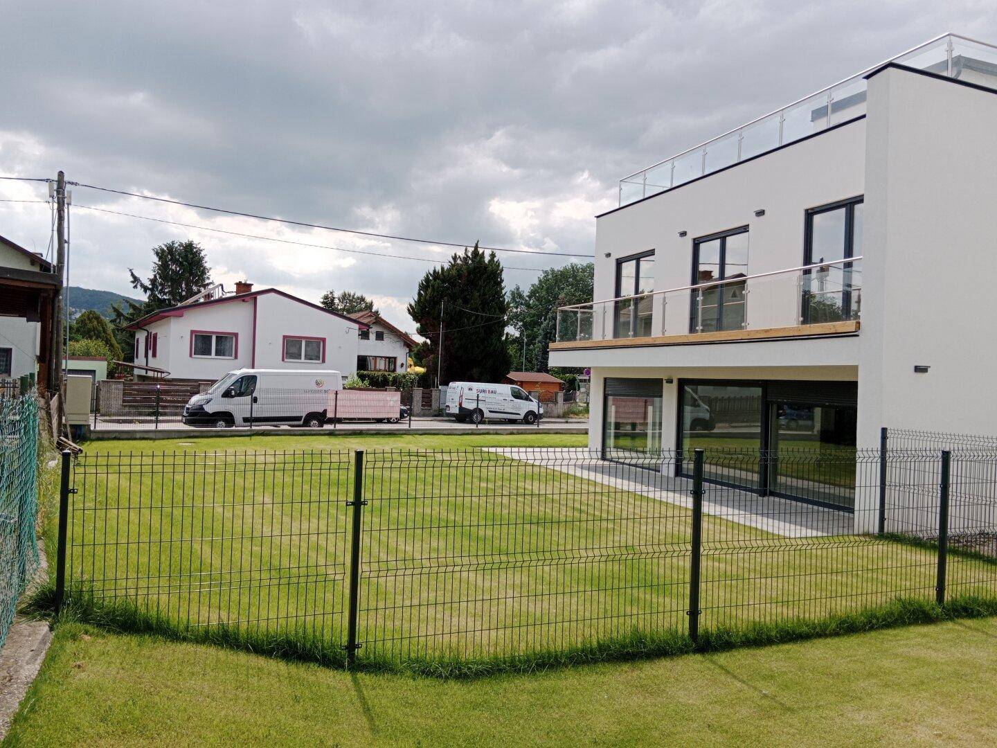 Seitenansicht des modernen Gebäudes mit Blick auf die Straße und benachbarte Häuser im ländlichen Umfeld.