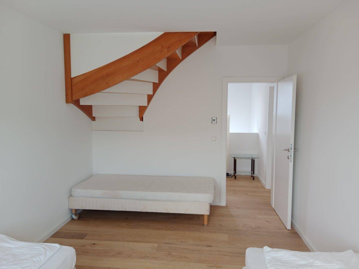 Helles Schlafzimmer mit Holzboden, weißen Wänden und offenem Treppenaufgang.