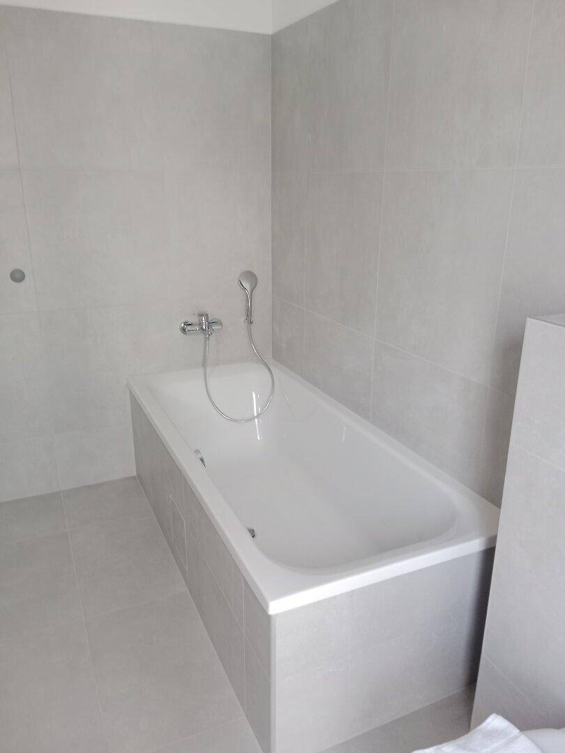 Modernes Badezimmer mit eingebauter Badewanne und durchgehend grauen Fliesen an Wänden und Boden.