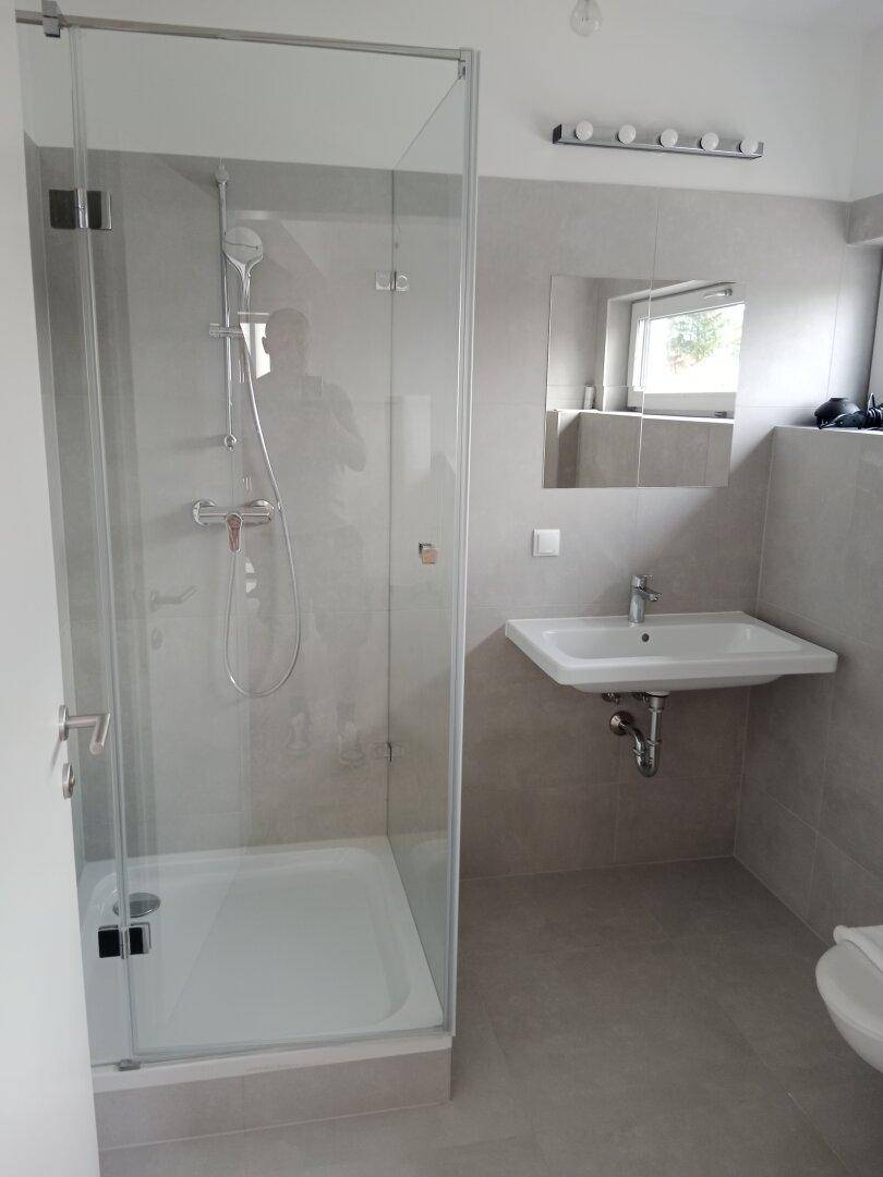 Helles Badezimmer mit moderner Duschkabine, Waschbecken und Fenster, komplett gefliest.