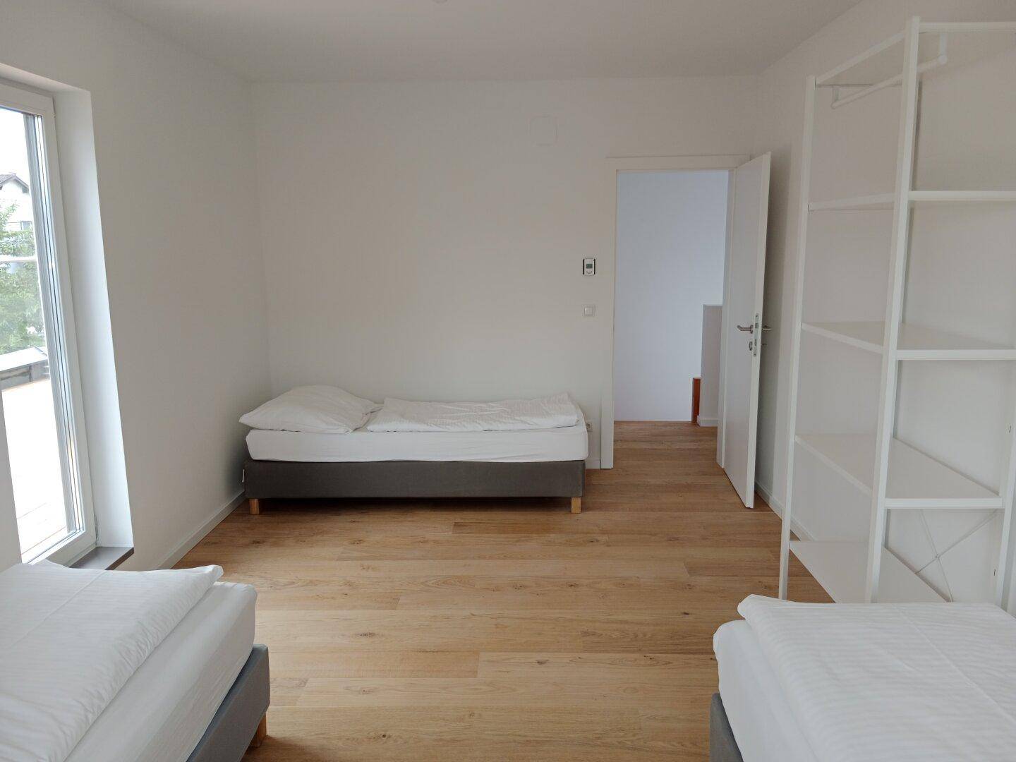 Geräumiges Schlafzimmer mit hellem Holzboden, weißen Wänden und großem Fenster für viel Tageslicht.