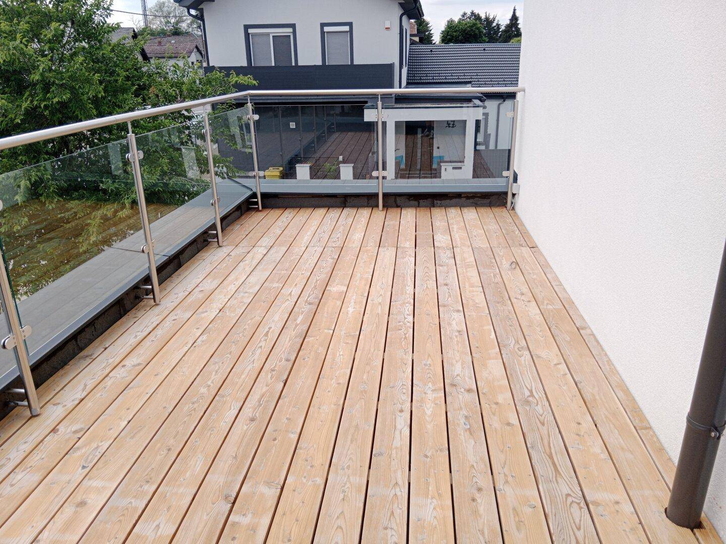 Große Holzterrasse mit modernem Glasgeländer, ideal für entspannte Stunden im Freien.
