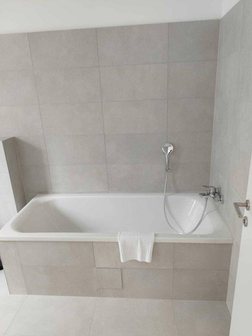Helles Badezimmer mit einer Badewanne, grauen Fliesen und einer modernen Armatur.