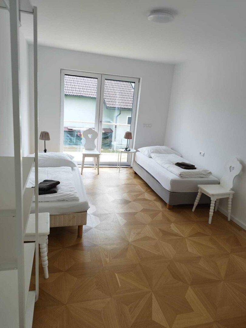Helles Schlafzimmer mit zwei Einzelbetten, Parkettboden und Zugang zu einem Fenster mit Blick ins Grüne.