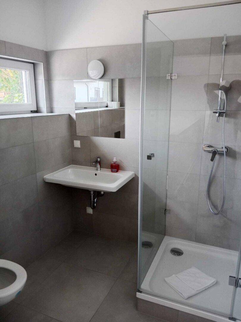 Modernes Badezimmer mit Duschkabine, Waschbecken, WC und Fenster für Tageslicht.