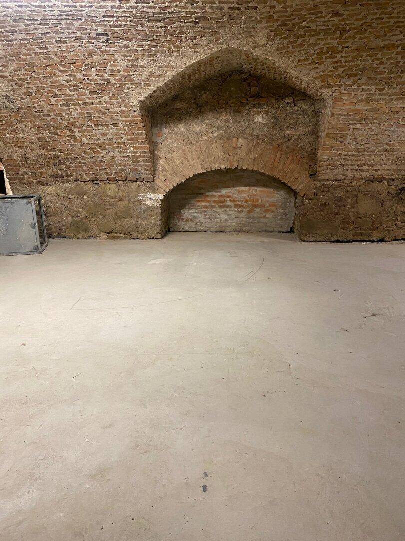 Detailansicht einer Ziegelwand im Keller mit einer gemauerten Nische und neuem Betonboden.