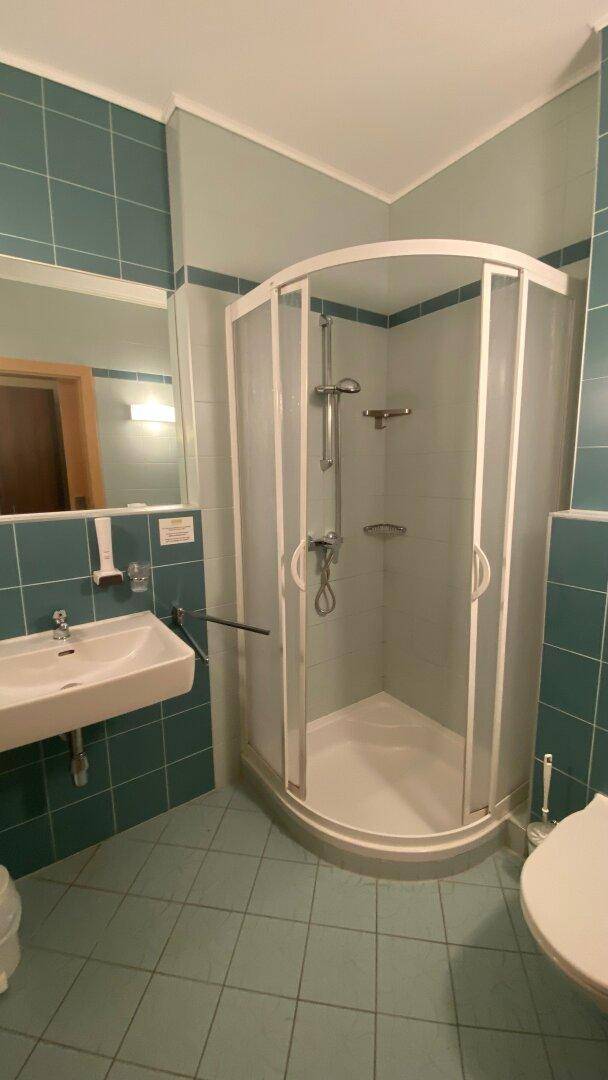 Badezimmer mit Eckduschkabine, Waschbecken und WC, ausgestattet mit hellblauen Fliesen.