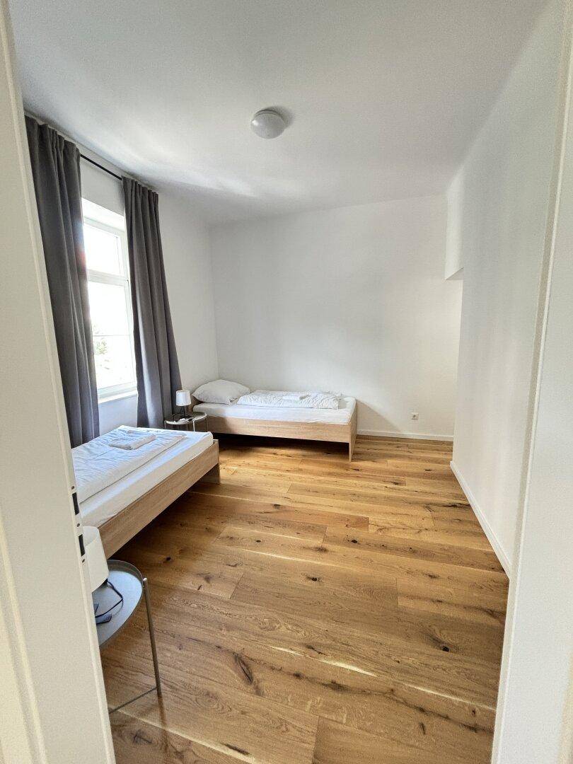 Schlafzimmer mit zwei Einzelbetten, Holzboden und natürlichem Lichteinfall.