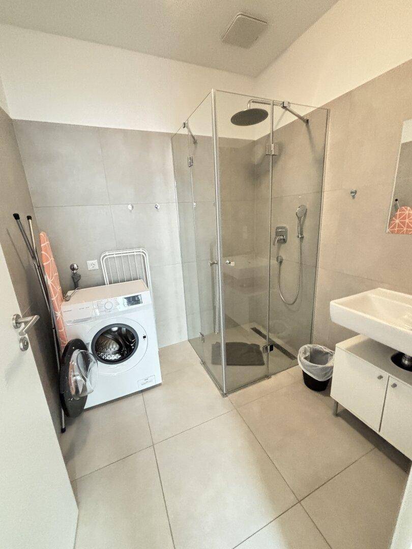 Modernes Badezimmer mit ebenerdiger Dusche, Waschbecken und Waschmaschine.