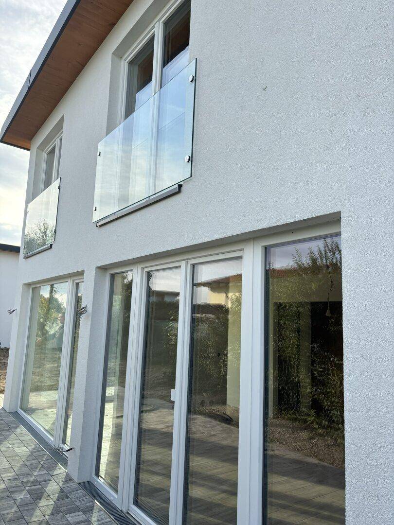 Detailansicht der modernen weißen Fassade mit bodentiefen Fenstern und Glasgeländer.