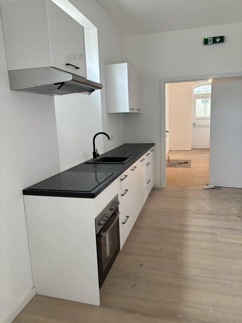 Moderne, neu installierte Küche mit weißen Schränken, schwarzer Arbeitsplatte und hellem Holzboden.