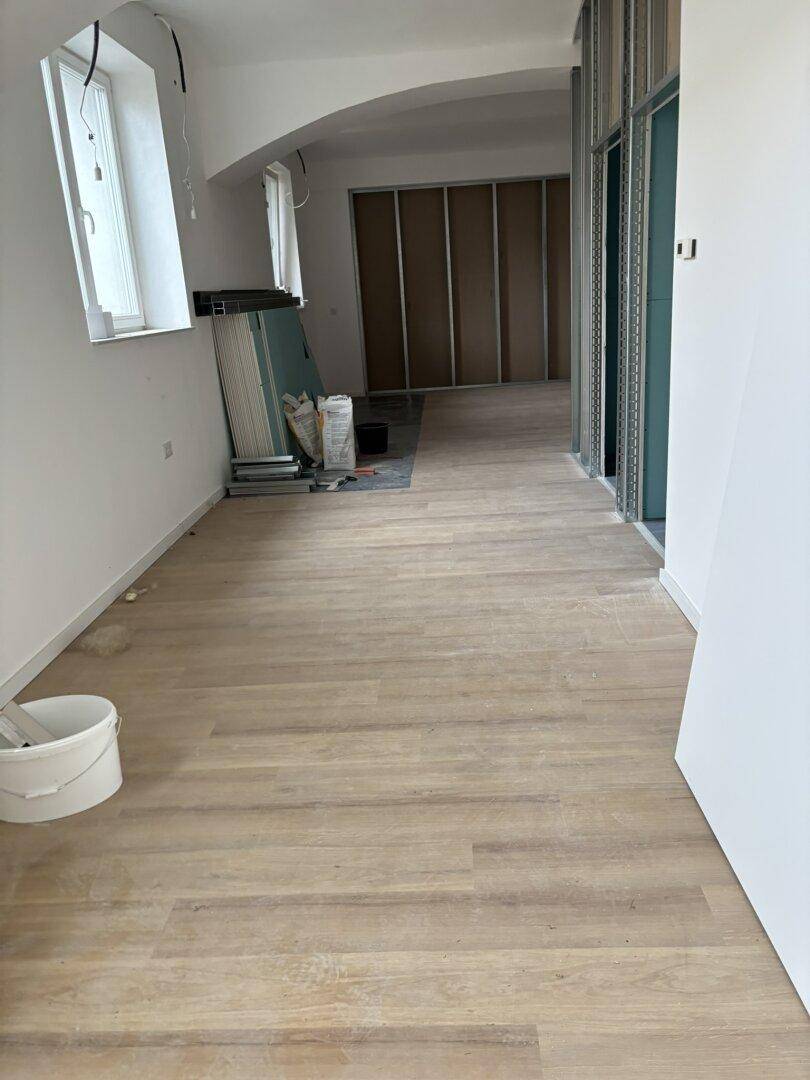 Großer, leerer Raum im Umbau mit hellem Holzboden und hohen, gewölbten Decken.