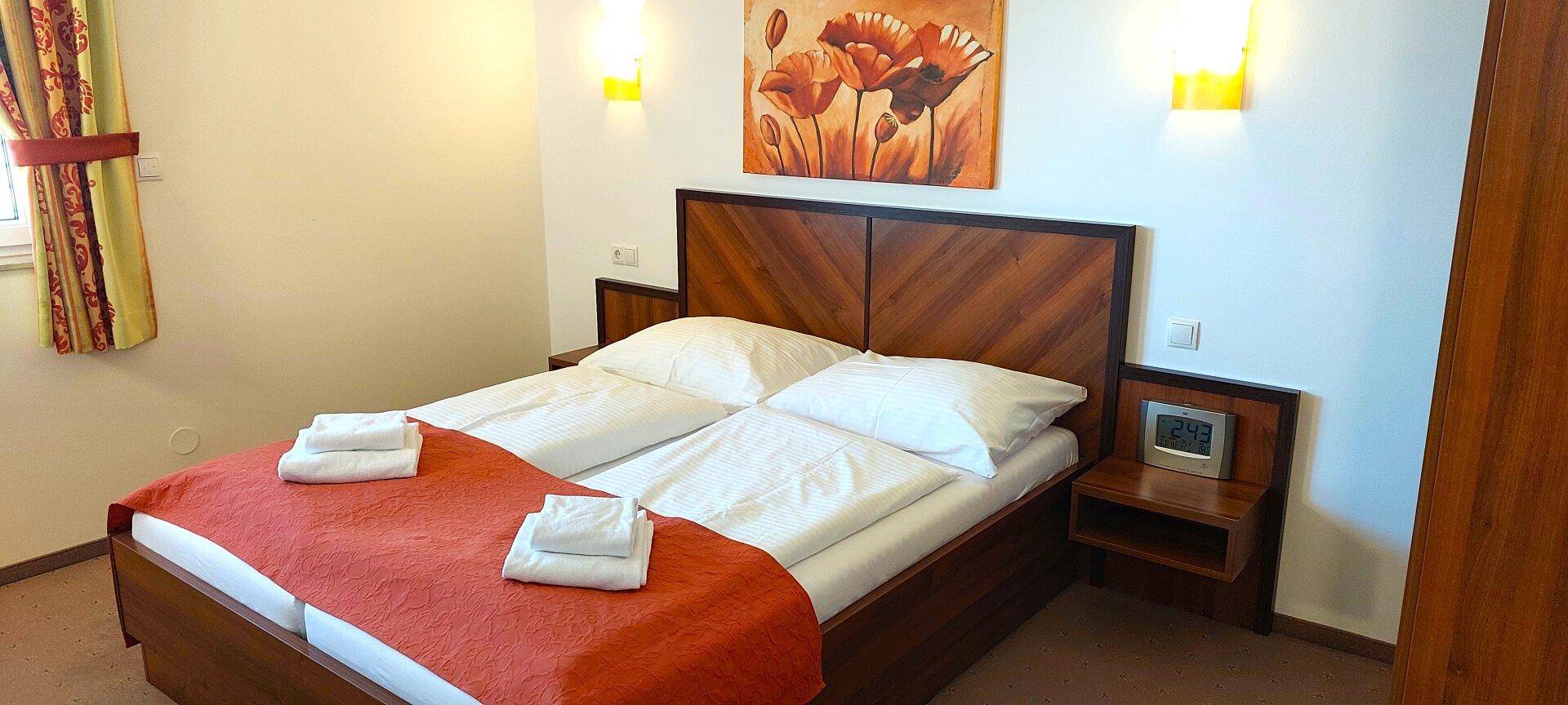 Gemütliches Schlafzimmer mit Doppelbett, Holzkopfteil und einem farbenfrohen Mohnblumenbild über dem Bett.