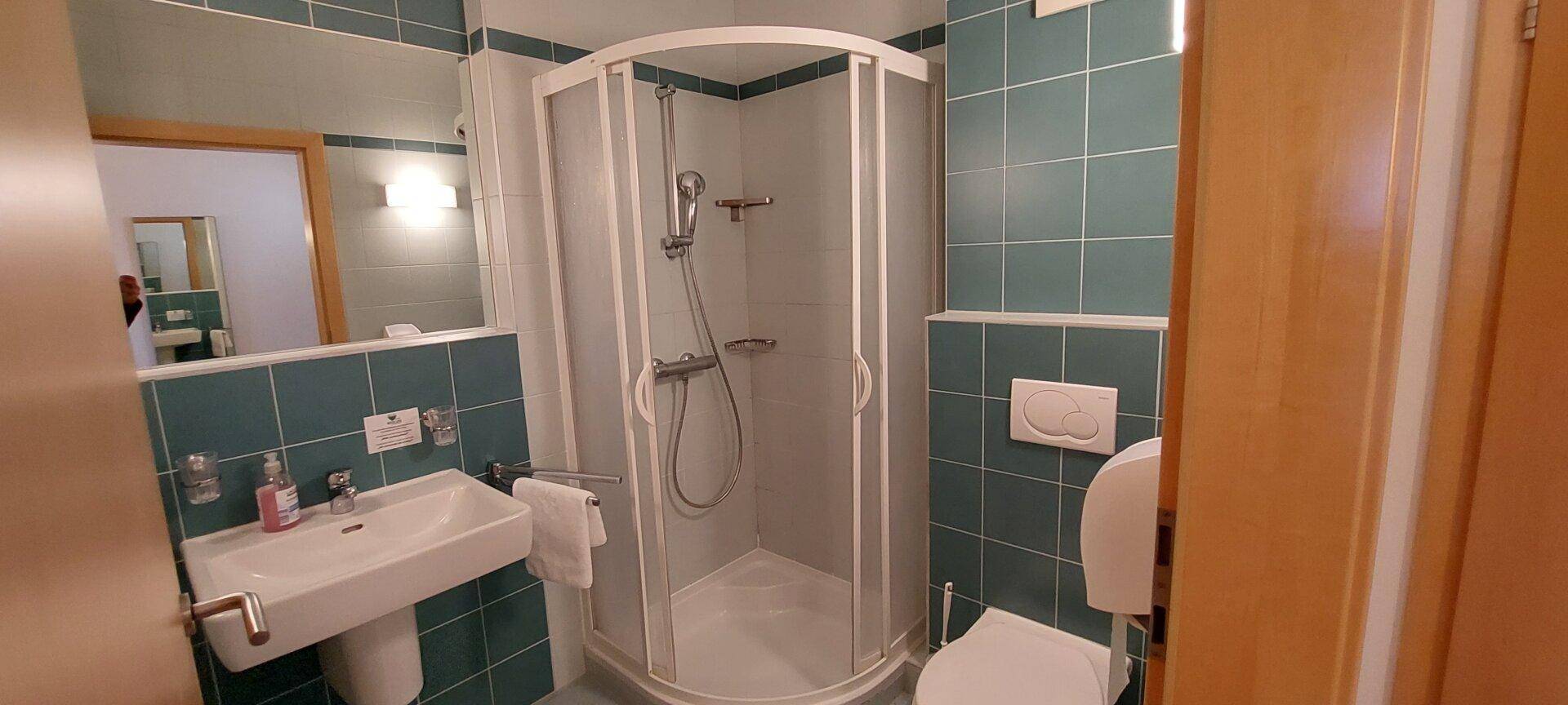 Badezimmer mit Duschkabine, Waschbecken und WC, ausgestattet mit blauen Fliesen.