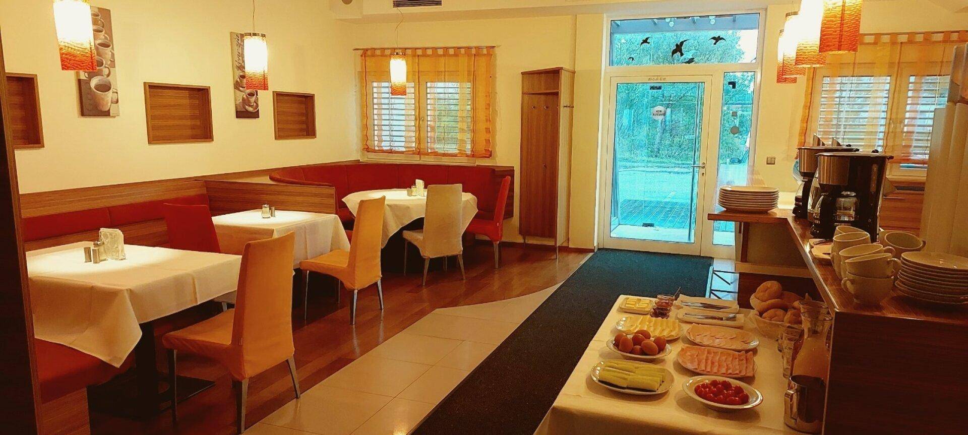 Gemütlicher Speisesaal mit Tischen, Stühlen und einem Frühstücksbuffet, mit Zugang zum Außenbereich.
