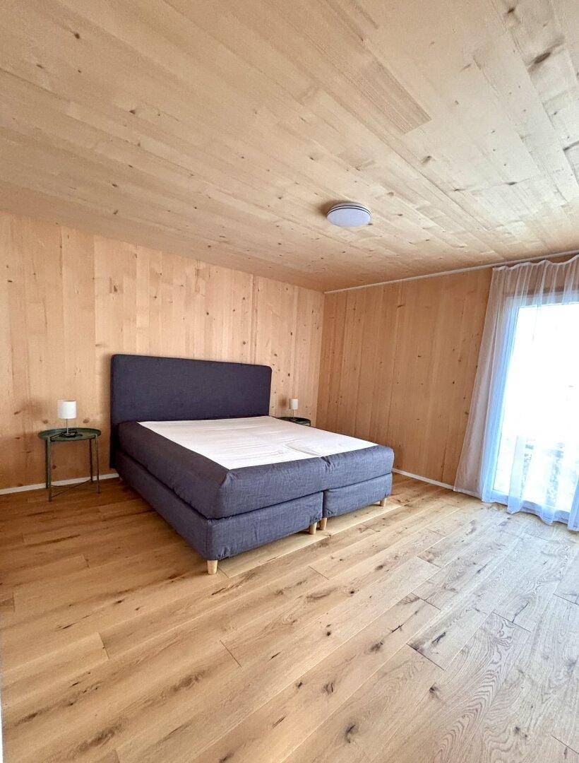 Helles Schlafzimmer mit Holzwänden, Holzdecke und Holzboden, ausgestattet mit einem modernen Bett.