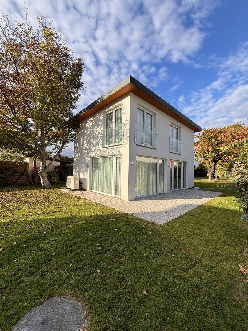 Rückansicht des modernen Hauses mit einer gepflasterten Terrasse und weitläufigem Rasenbereich.