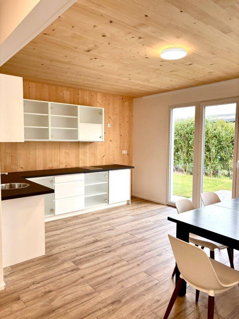 Helle Küche mit weißen Schränken und dunklen Arbeitsplatten, mit Zugang zum Garten durch große Glastüren.
