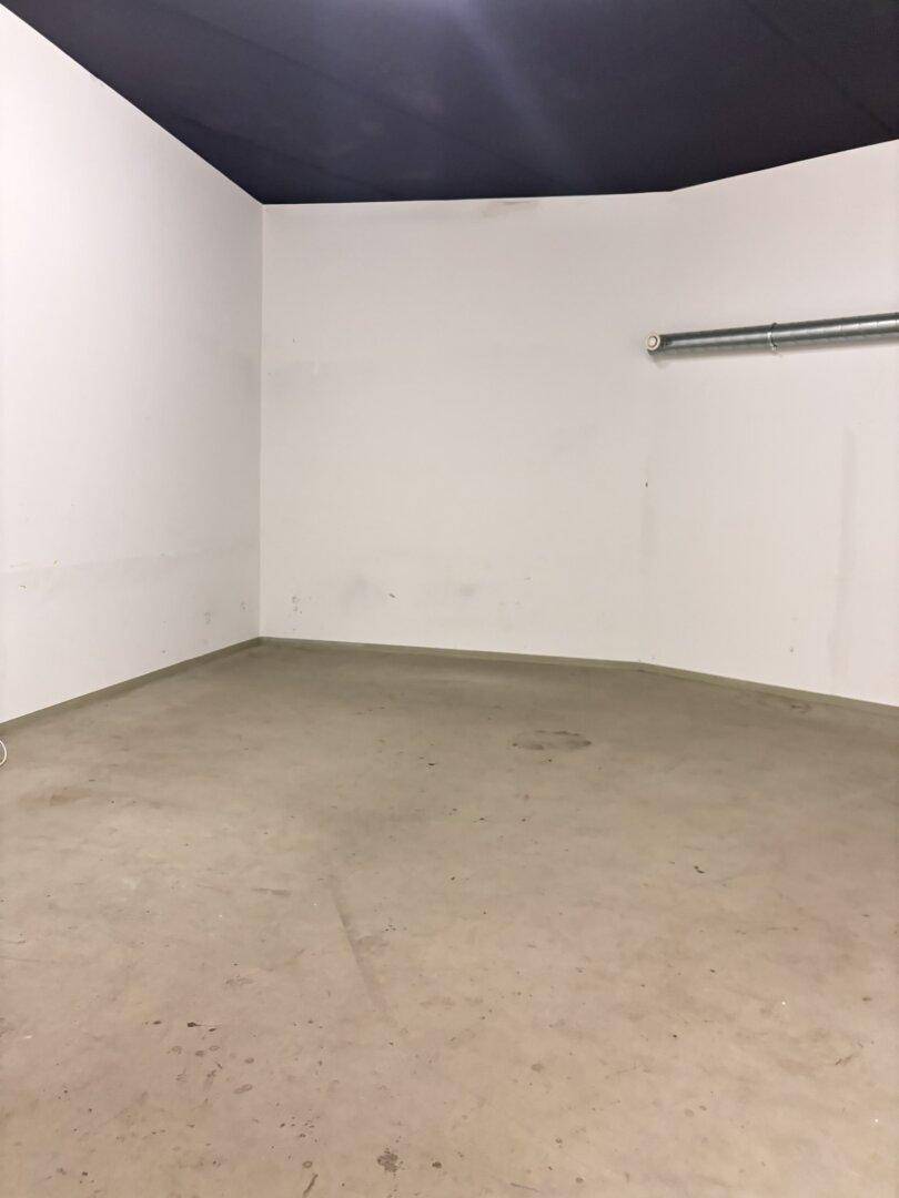 Leerer Raum mit Betonboden, weißen Wänden und dunkler Decke, ideal als Lagerfläche.