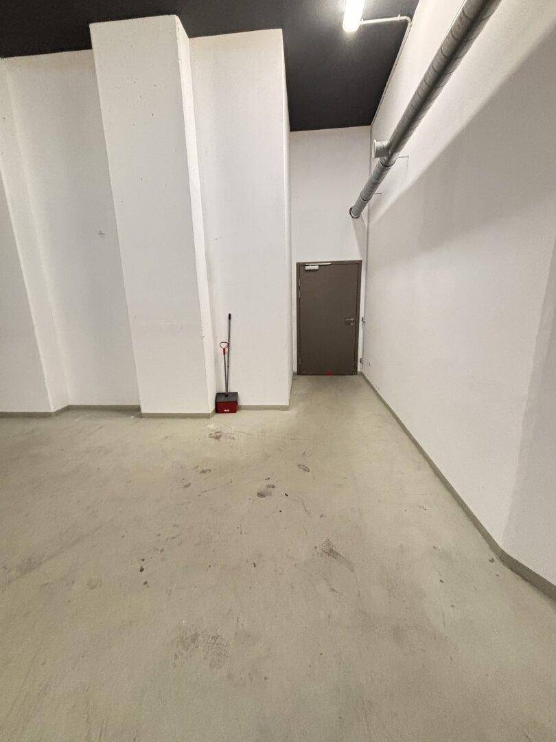 Leerer Raum mit Betonboden, weißen Wänden, dunkler Decke und einer einfachen Tür.