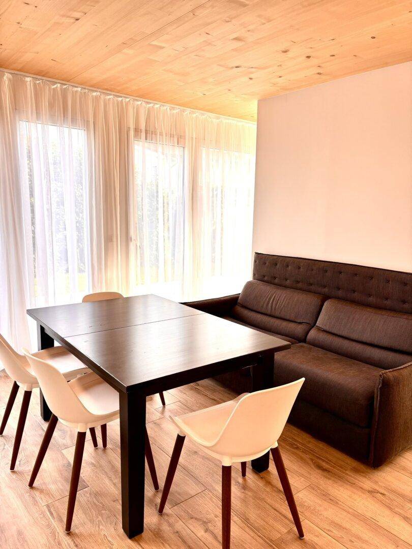 Gemütlicher Essbereich mit Holztisch, modernen Stühlen und Sofa, umgeben von Holzelementen.