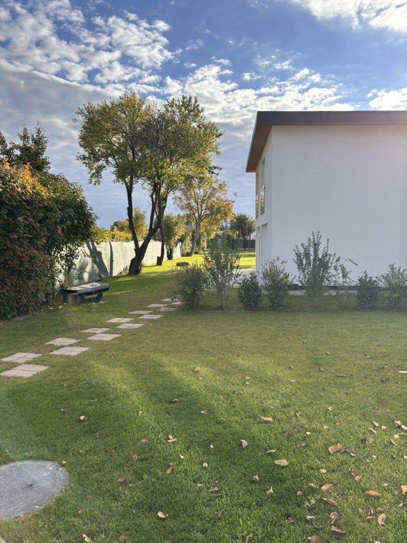 Weitläufiger Garten mit Rasen, einem Steinweg und einer Holzbank unter Bäumen.