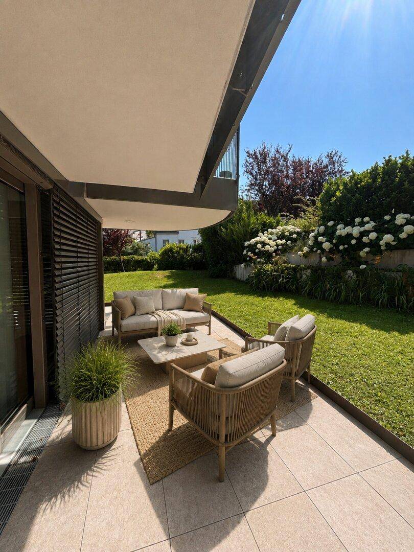 Sonnige Terrasse mit bequemen Outdoor-Möbeln und Blick auf den gepflegten Garten.