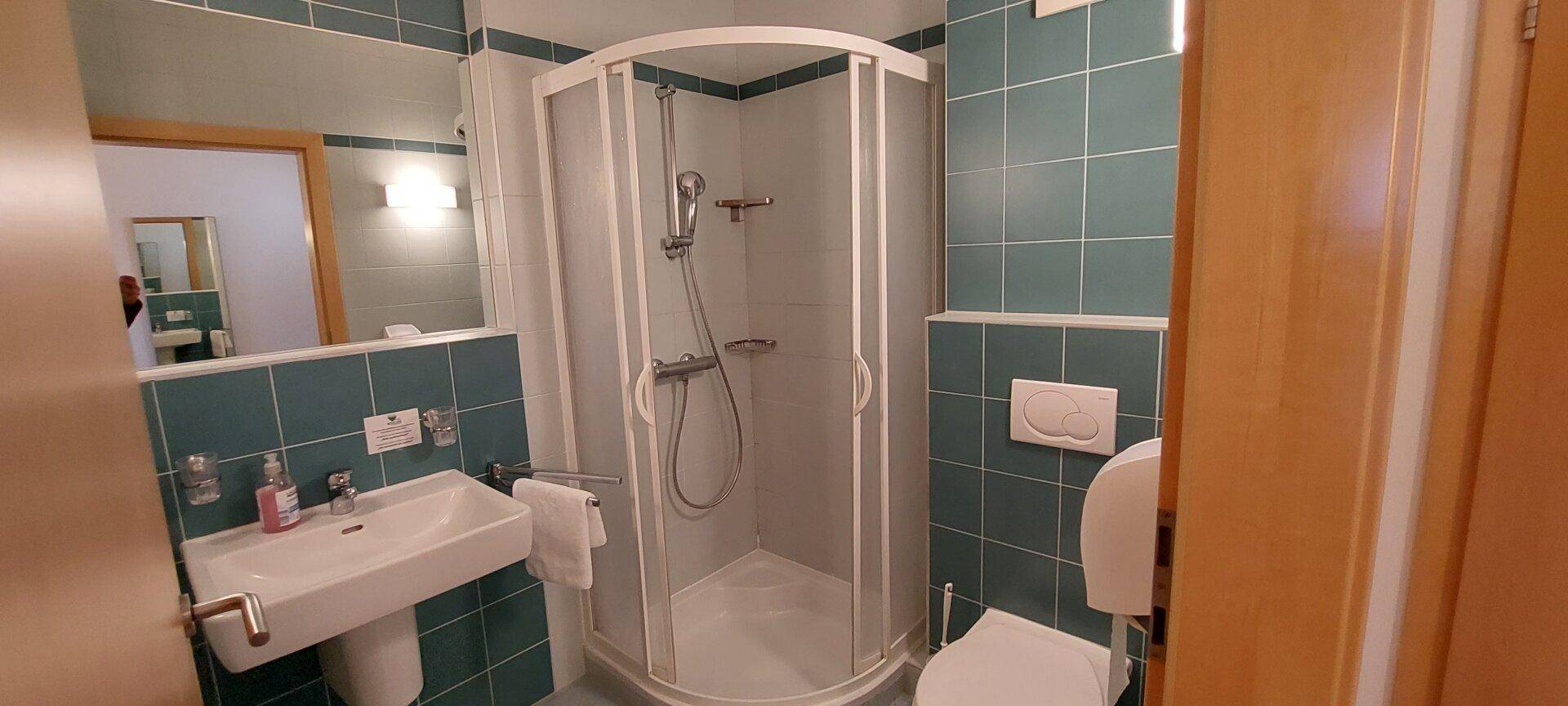 Funktionales Badezimmer mit Duschkabine, Waschbecken und WC in grünen Fliesen.