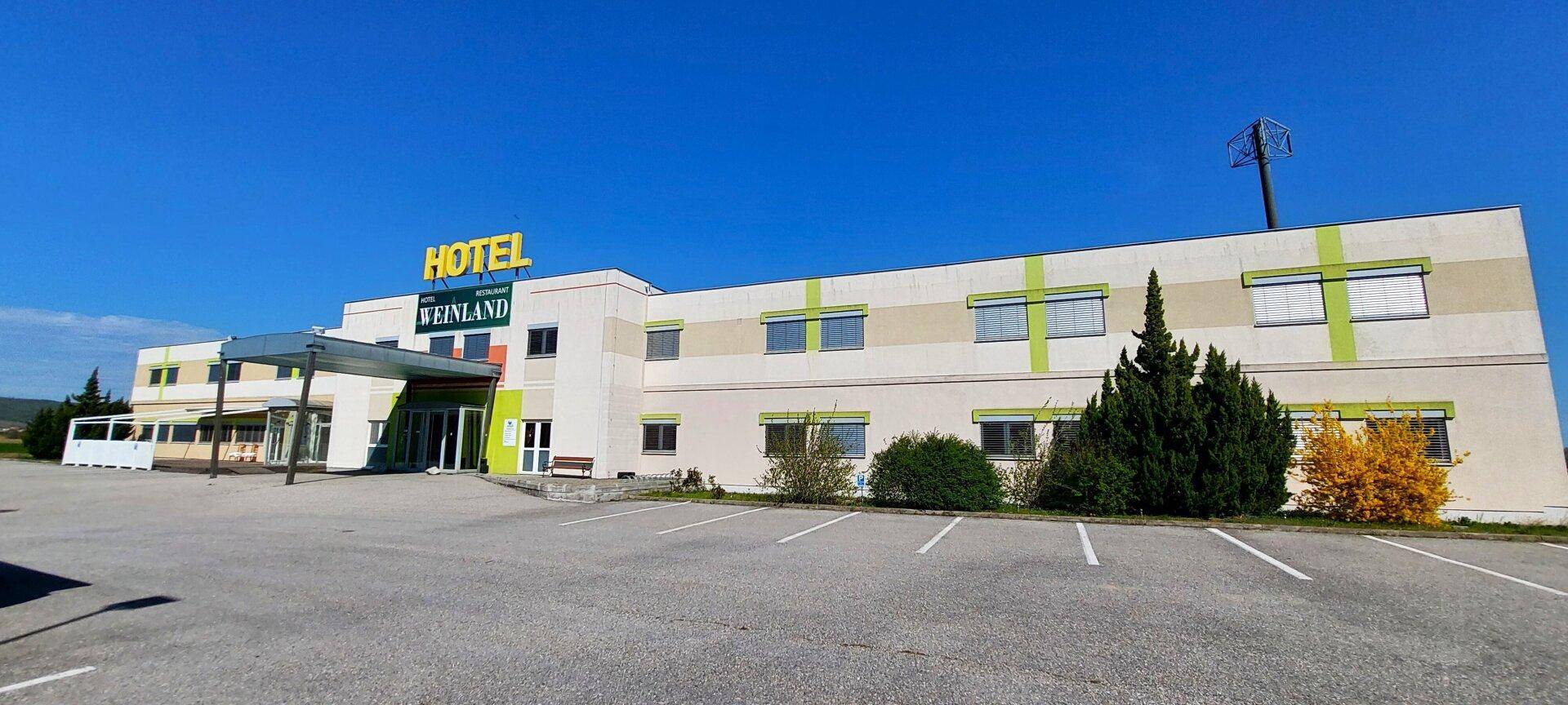 Außenansicht eines Hotels mit großem Parkplatz unter blauem Himmel.