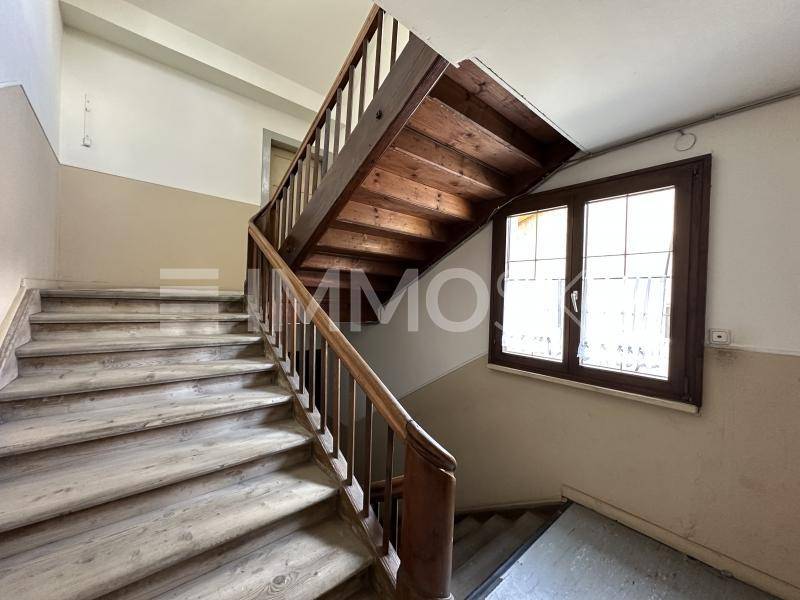 Helles Treppenhaus mit Holztreppe und Holzgeländer, beleuchtet durch ein Fenster.