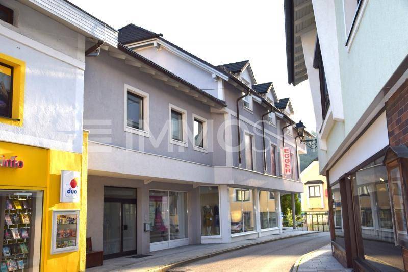 Gebäudeansicht entlang einer Gasse mit Schaufenstern im Erdgeschoss und Wohnungen darüber.