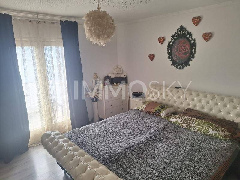 Helles Schlafzimmer mit großem Fenster, Doppelbett und dekorativen Elementen.