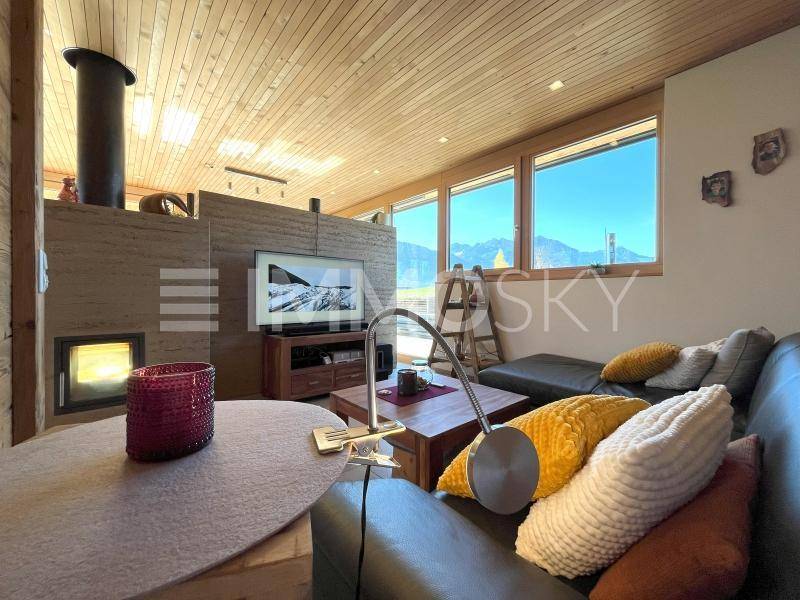 Gemütliches Wohnzimmer mit Holzbalkendecke, Kaminofen und großen Fenstern mit Bergblick.
