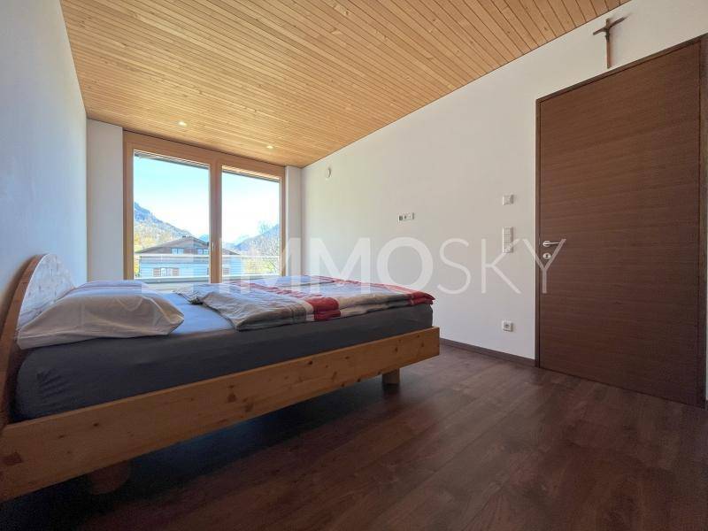 Gemütliches Schlafzimmer mit Holzbett, Holzbalkendecke und großen Fenstern mit Bergblick.
