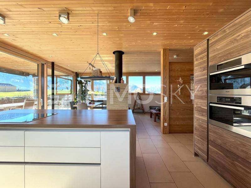 Moderne offene Küche mit Holzelementen, Kochinsel und Zugang zur Terrasse mit Bergblick.