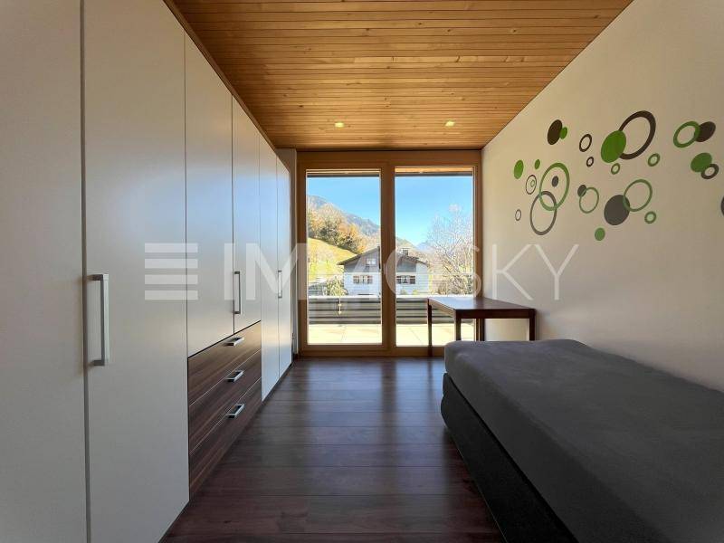 Helles Schlafzimmer mit Einbauschränken, Holzbalkendecke und großen Fenstern mit Blick ins Grüne.