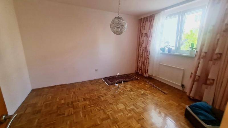 Leeres Schlafzimmer mit Parkettboden, großem Fenster und einer modernen Deckenleuchte.