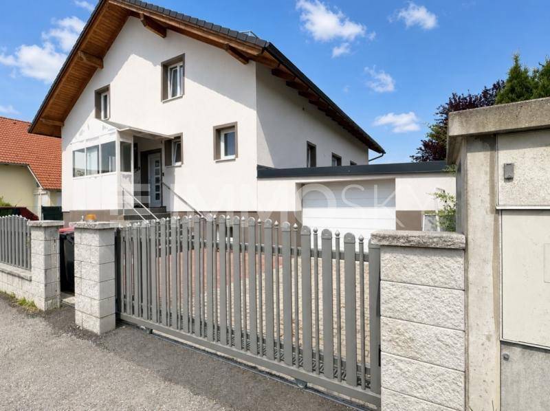 Vorderansicht des Hauses mit Einfahrtstor, Zaun und integrierter Garage unter blauem Himmel.