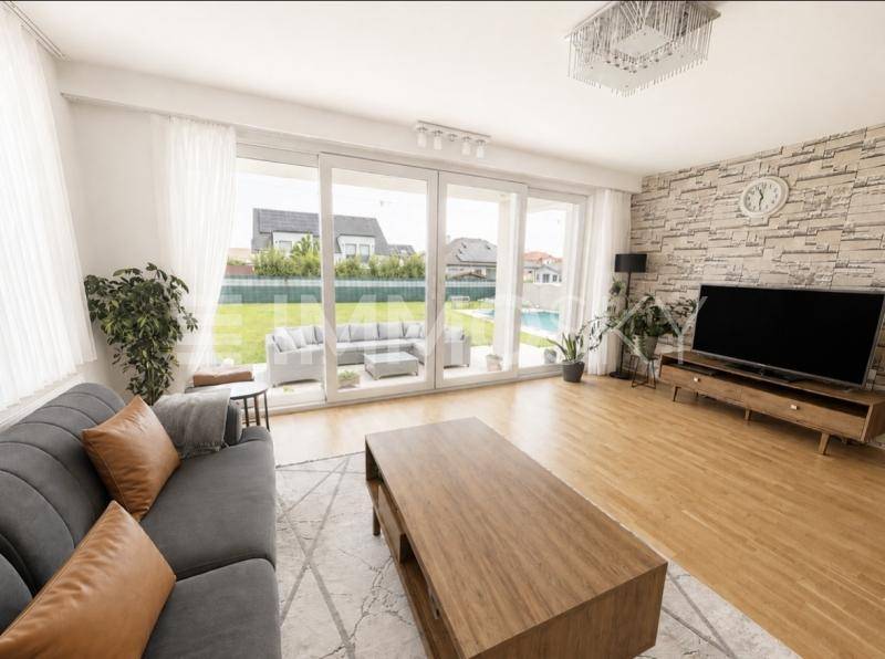 Helles Wohnzimmer mit bequemer Couch, Holztisch und großen Schiebetüren zum Garten mit Pool.