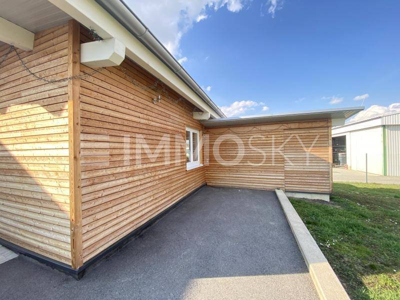 Holzverkleidete Fassade des Gebäudes mit einem kleinen gepflasterten Bereich daneben.
