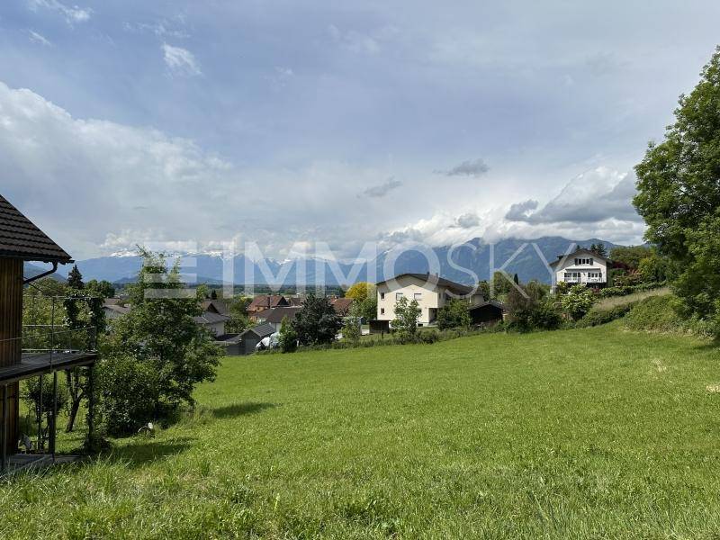Weitläufige grüne Landschaft mit Häusern und einem Panoramablick auf die fernen Berge.
