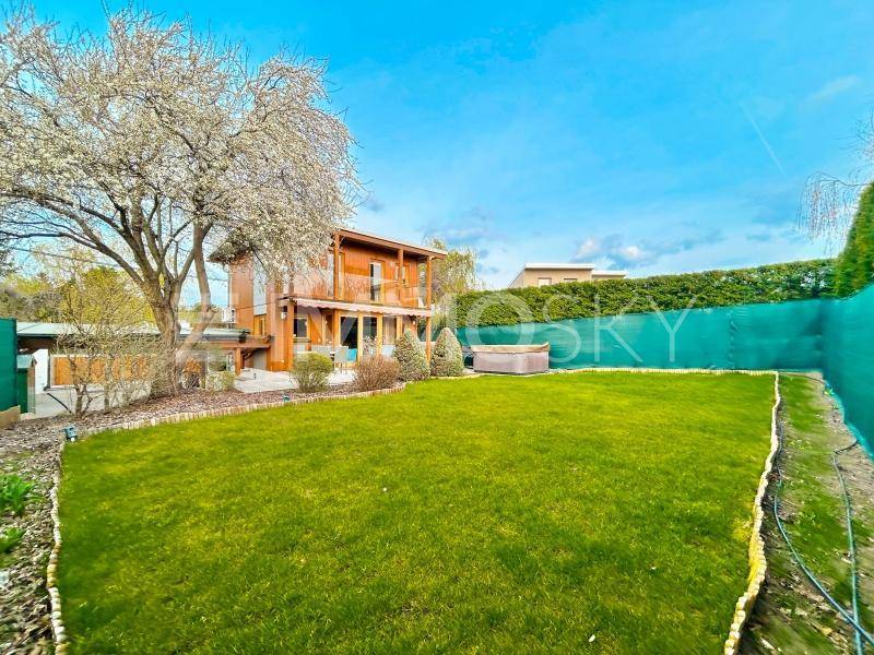 Großer, gepflegter Garten mit Rasenfläche, Bäumen und Blick auf das moderne Holzhaus.