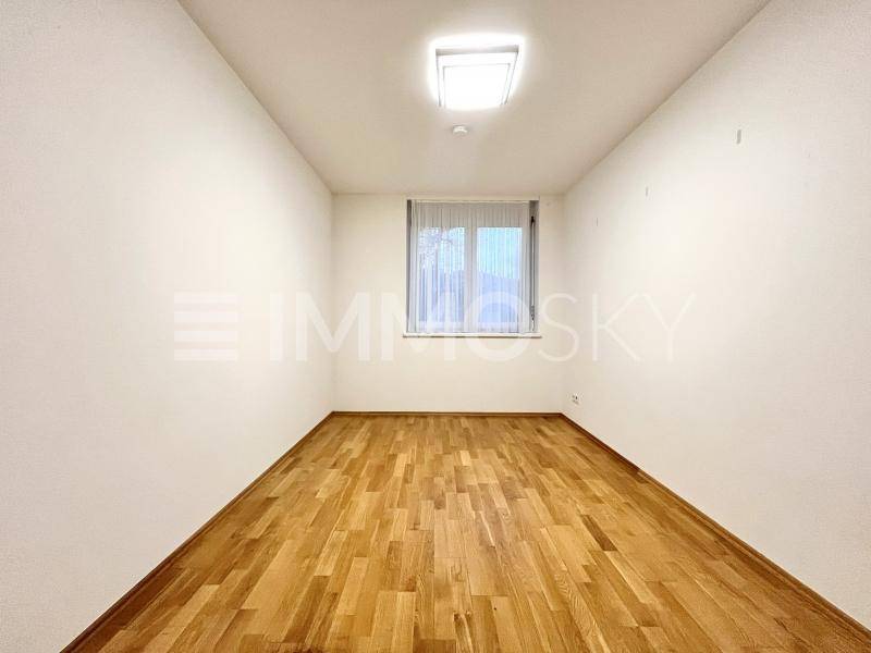 Helles, leeres Zimmer mit Holzparkett und einem Fenster, ideal als Schlaf- oder Arbeitszimmer.